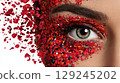 Woman with eye makeup decorated with red glitter and confetti creating a vibrant, artistic look 129245202