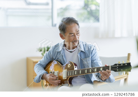 A man in his 60s playing an electric guitar 129245786
