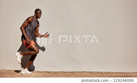 Athletic man running outdoors against a blank wall under sunlight Athletic man running outdoors against a blank wall under sunlight 129246000
