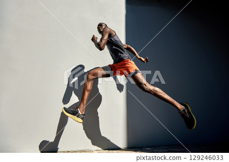 Athletic man running outdoors against a neutral background with dramatic lighting Athletic man running outdoors against a neutral background with dramatic lighting 129246033