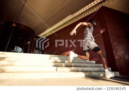 Athletic man sprinting up stairs with determination and energy outdoors Athletic man sprinting up stairs with determination and energy outdoors 129246145