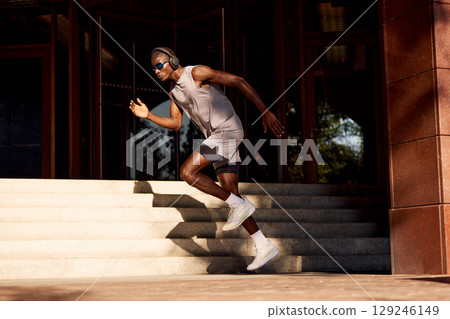 Athletic man running outdoors next to building in evening sunlight Athletic man running outdoors next to building in evening sunlight 129246149