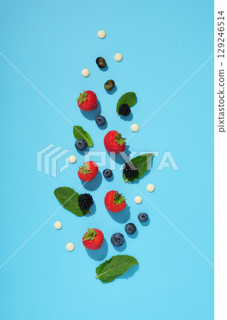 Scattered fresh berries, mint leaves, and white chocolate drops on a bright blue background. Healthy summer ingredients. 129246514