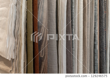 A collection of various fabric swatches in neutral tones. The fabrics include linen, cotton, and silk, arranged neatly in vertical rows. 129246575