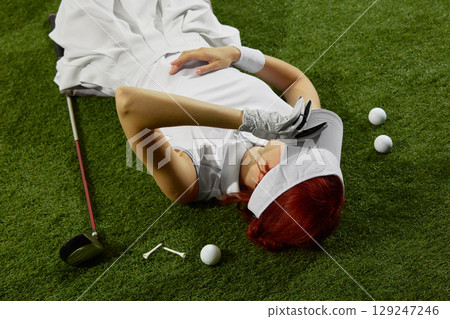 Woman lying on golf field with glove and visor Woman lying on golf field with glove and visor 129247246