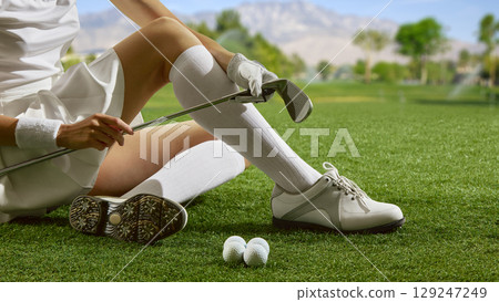 Woman sitting on grass with golf club and balls 129247249