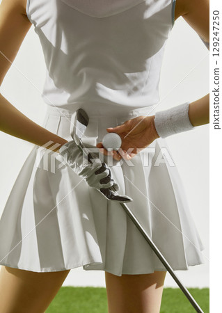 Woman in white golf outfit holding ball and iron club Woman in white golf outfit holding ball and iron club 129247250
