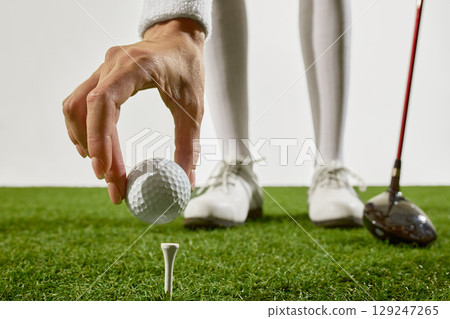 Hand placing golf ball on tee with player shoes in background Hand placing golf ball on tee with player shoes in background 129247265