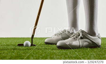 Close-up of golf shoes and putter on green grass 129247270