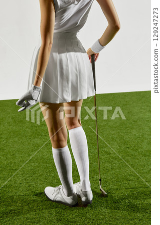 Rear view of woman golfer in white skirt standing with club on green 129247273