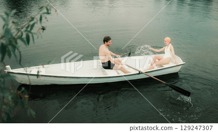 Man and woman laughing and splashing water while rowing boat on river Man and woman laughing and splashing water while rowing boat on river 129247307
