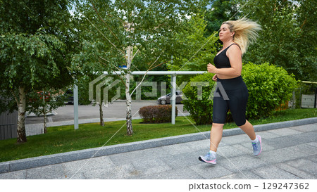Woman jogging in black activewear through green city park zone Woman jogging in black activewear through green city park zone 129247362