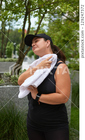Woman in black cap cooling off after workout with towel in urban park Woman in black cap cooling off after workout with towel in urban park 129247372