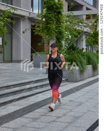 Woman jogging in city area wearing black cap and colorful leggings Woman jogging in city area wearing black cap and colorful leggings 129247408