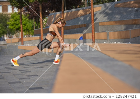 Woman performing stretches outside during workout on sunny day Woman performing stretches outside during workout on sunny day 129247421