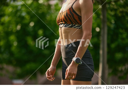Fit woman in zebra sports bra and shorts standing in park with toned abs Fit woman in zebra sports bra and shorts standing in park with toned abs 129247423