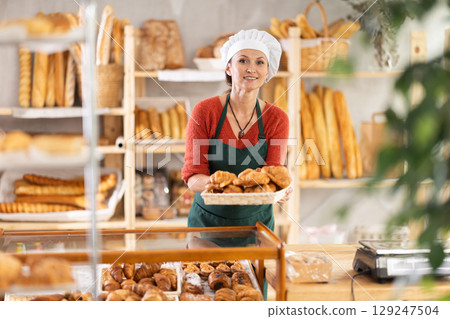 Portrait of positive woman bakery worker with croissants 129247504