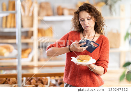 Woman photographing burger in bakery Woman photographing burger in bakery 129247512