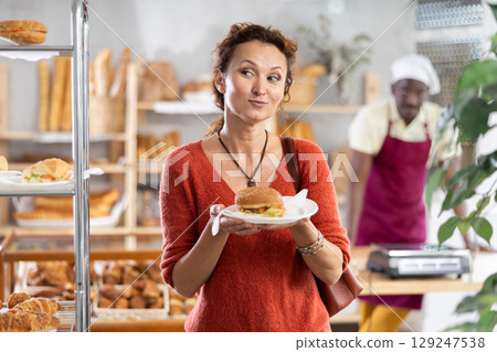 Cheerful woman with just cooked tasty hamburger in bakery 129247538