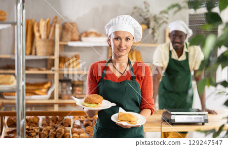 Female baker in apron offers to buy fresh hot dogs, pies and burgers 129247547