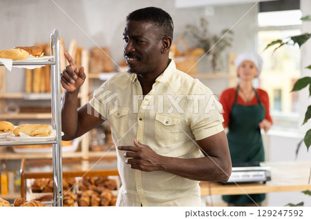 African man near window of bakery food court store examines assortment African man near window of bakery food court store examines assortment 129247592