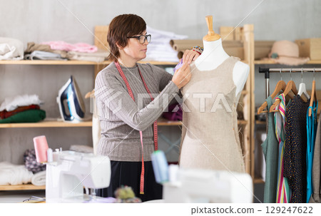 Seamstress shaping dress on mannequin in tailoring studio Seamstress shaping dress on mannequin in tailoring studio 129247622