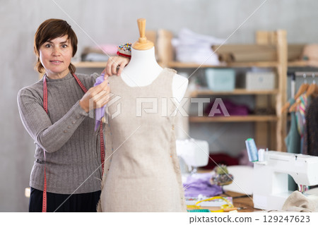 Seamstress shaping dress on mannequin in tailoring studio Seamstress shaping dress on mannequin in tailoring studio 129247623
