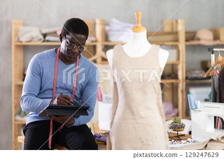 African American man tailor creates sketch of dress on tablet African American man tailor creates sketch of dress on tablet 129247629