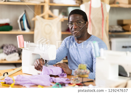 Experienced tailor using sewing machine to make garment in studio Experienced tailor using sewing machine to make garment in studio 129247637