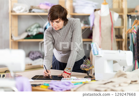 Female dressmaker working on digital sketch of dress in workshop 129247668