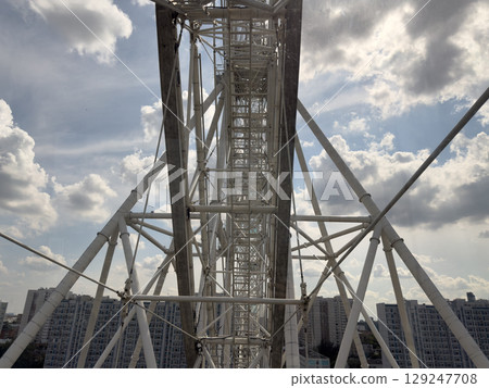 Close up of the steel structure of Ferris wheel, showing the intricate frame and supporting beams against the city skyline and cloud filled sky Close up of the steel structure of Ferris wheel, showing the intricate frame and supporting beams against the city skyline and cloud filled sky 129247708