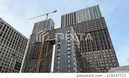 Construction site of two tall residential buildings under development, with scaffolding and crane, showcasing the modern building process and urban architecture in progress Construction site of two tall residential buildings under development, with scaffolding and crane, showcasing the modern building process and urban architecture in progress 129247722