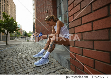 Athletic woman resting on urban steps with water bottle after run Athletic woman resting on urban steps with water bottle after run 129247797