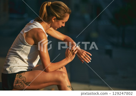 Woman in sportswear observes her fitness watch post urban outdoor exercise 129247802