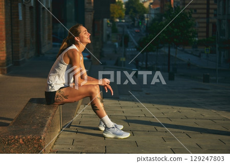 Young woman runner resting on urban street during sunset, enjoying peaceful atmosphere Young woman runner resting on urban street during sunset, enjoying peaceful atmosphere 129247803