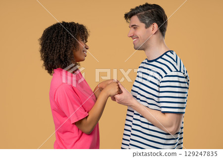 Love confession. Happy interracial couple stands on beige, holding hands Love confession. Happy interracial couple stands on beige, holding hands 129247835