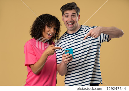 Interracial Couple Pointing to Mobile.Woman Man Smiling With Smartphone on Beige 129247844