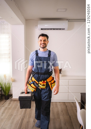 Technician smiling and walking carrying toolbox and wearing tool belt in a house 129248084