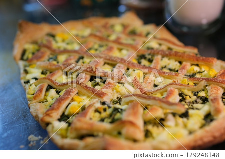 A slice of baked savory pastry with a lattice top and spinach filling sits on a colorful plate against a wooden surface A slice of baked savory pastry with a lattice top and spinach filling sits on a colorful plate against a wooden surface 129248148