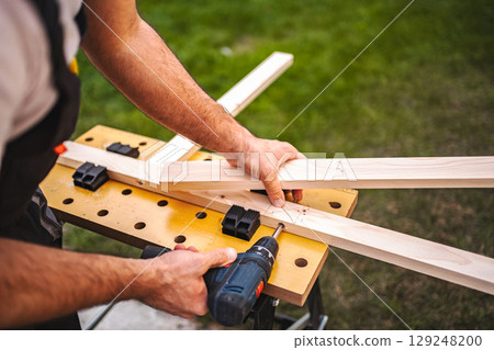 Unrecognizable male carpenter using electric screwdriver on a wooden plank outdoors 129248200
