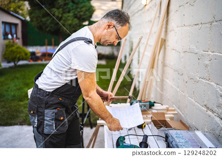 Mature male carpenter working with wooden plank outdoors 129248202