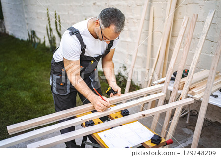 Mature male carpenter measuring wooden plank outdoors 129248209