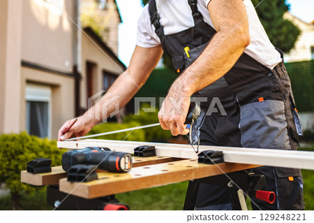 Unrecognizable male carpenter measuring wooden plank outdoors 129248221