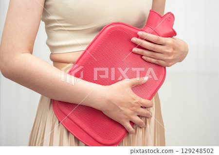 Woman using hot water bottle to relieve menstrual abdominal pain. 129248502