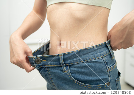 Young Asian woman losing weight wearing loose pants in oversize jeans. 129248508