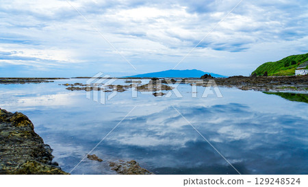 Under cloudy skies, the sky is reflected on the rocks at low tide at Manjojiki on Sado Island. 129248524