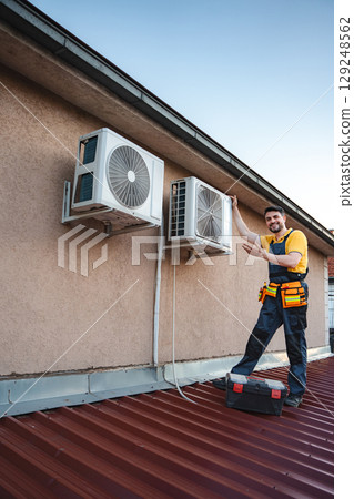 HVAC technician installing an air conditioner on a building rooftop 129248562