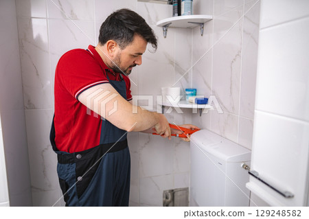 Plumber repairing toilet cistern in bathroom using pliers Plumber repairing toilet cistern in bathroom using pliers 129248582