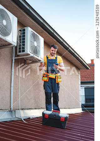Technician checking air conditioning outdoor unit on the roof Technician checking air conditioning outdoor unit on the roof 129248589
