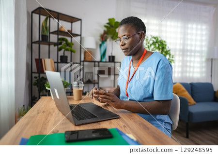 Focused african american female doctor working on a laptop at home 129248595
